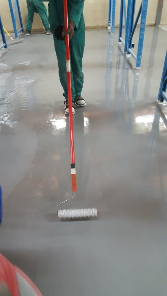 APR Waterproofing technicians applying epoxy coating on an indoor floor while wearing safety gear.