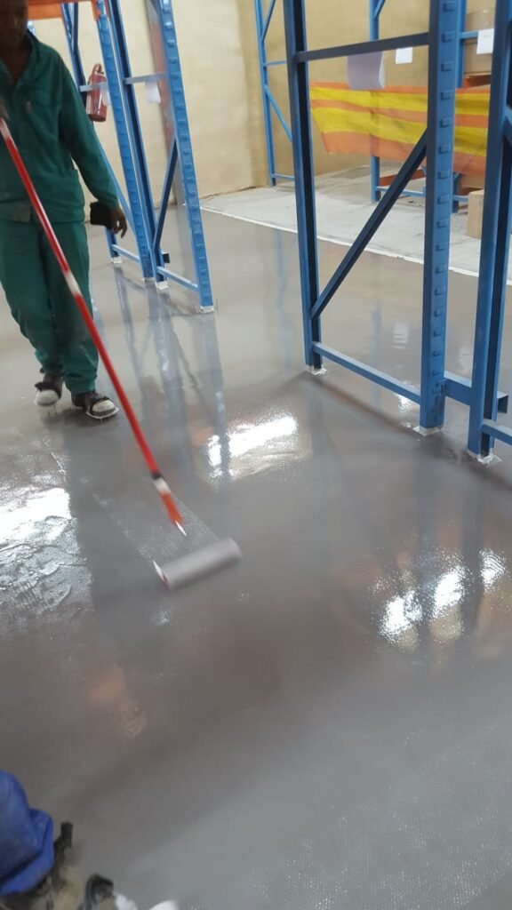 APR Waterproofing workers applying epoxy paint on an indoor floor during the painting process.