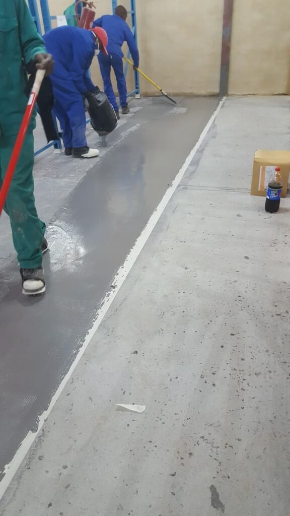 APR Waterproofing workers wearing protective equipment while applying epoxy coating on an indoor floor.