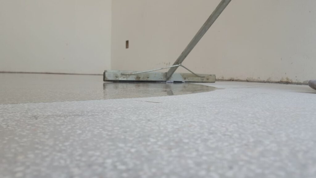 Close-up of APR Waterproofing technicians applying epoxy coating on an indoor floor while wearing protective gear.