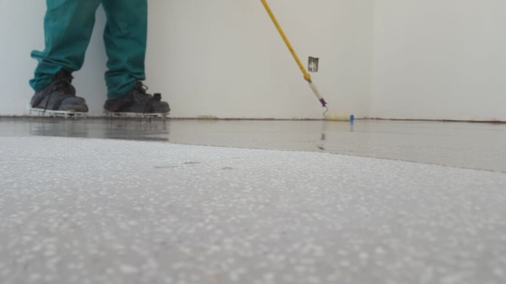 Close-up of APR Waterproofing technicians applying epoxy coating on an indoor floor while wearing safety gear.